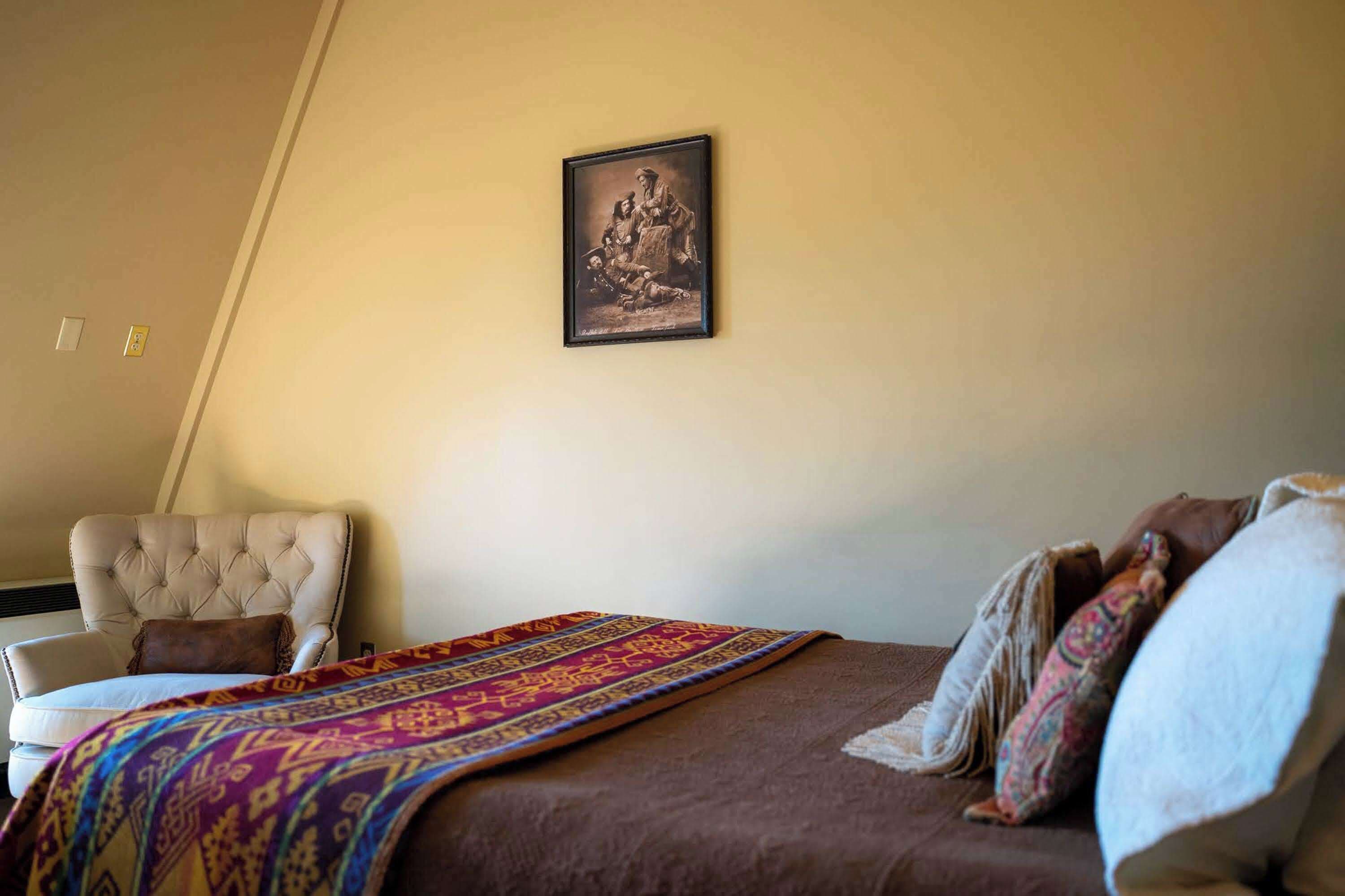 A bedroom with a bed, a chair, and a framed picture on the wall.