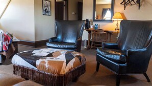 A room with two leather armchairs, a patterned ottoman, a coffee table, a mirror, and a coat rack. - Sheridan Inn, B/W Signature Collection (Sheridan)