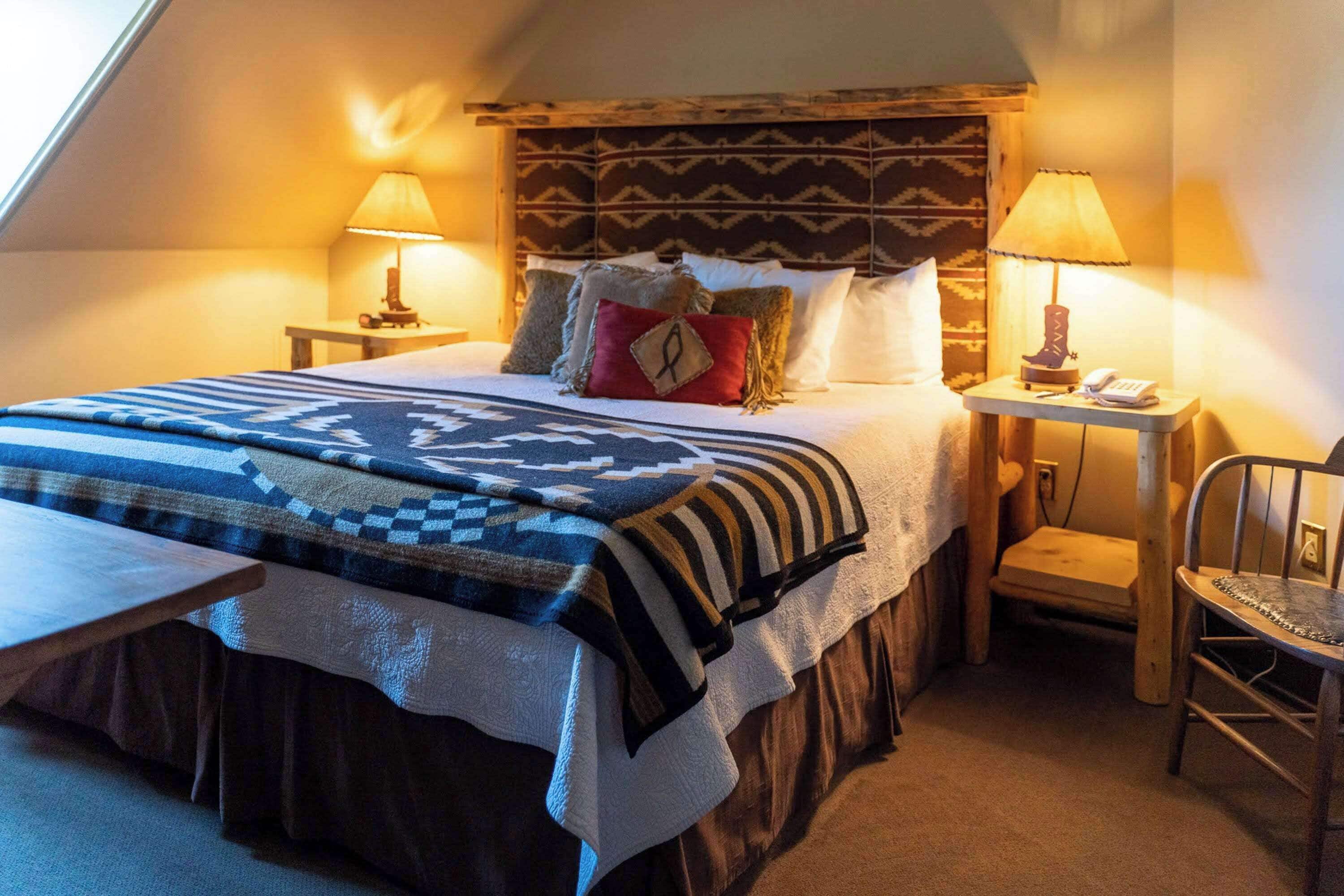Een gezellige, goed verlichte slaapkamer met een groot bed, twee nachtkastjes met lampen, een houten hoofdbord en een kleine houten stoel.