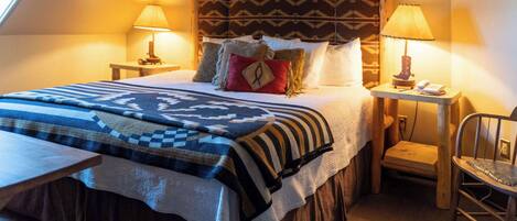 A cozy, well-lit bedroom with a large bed, two bedside tables with lamps, a wooden headboard, and a small wooden chair.