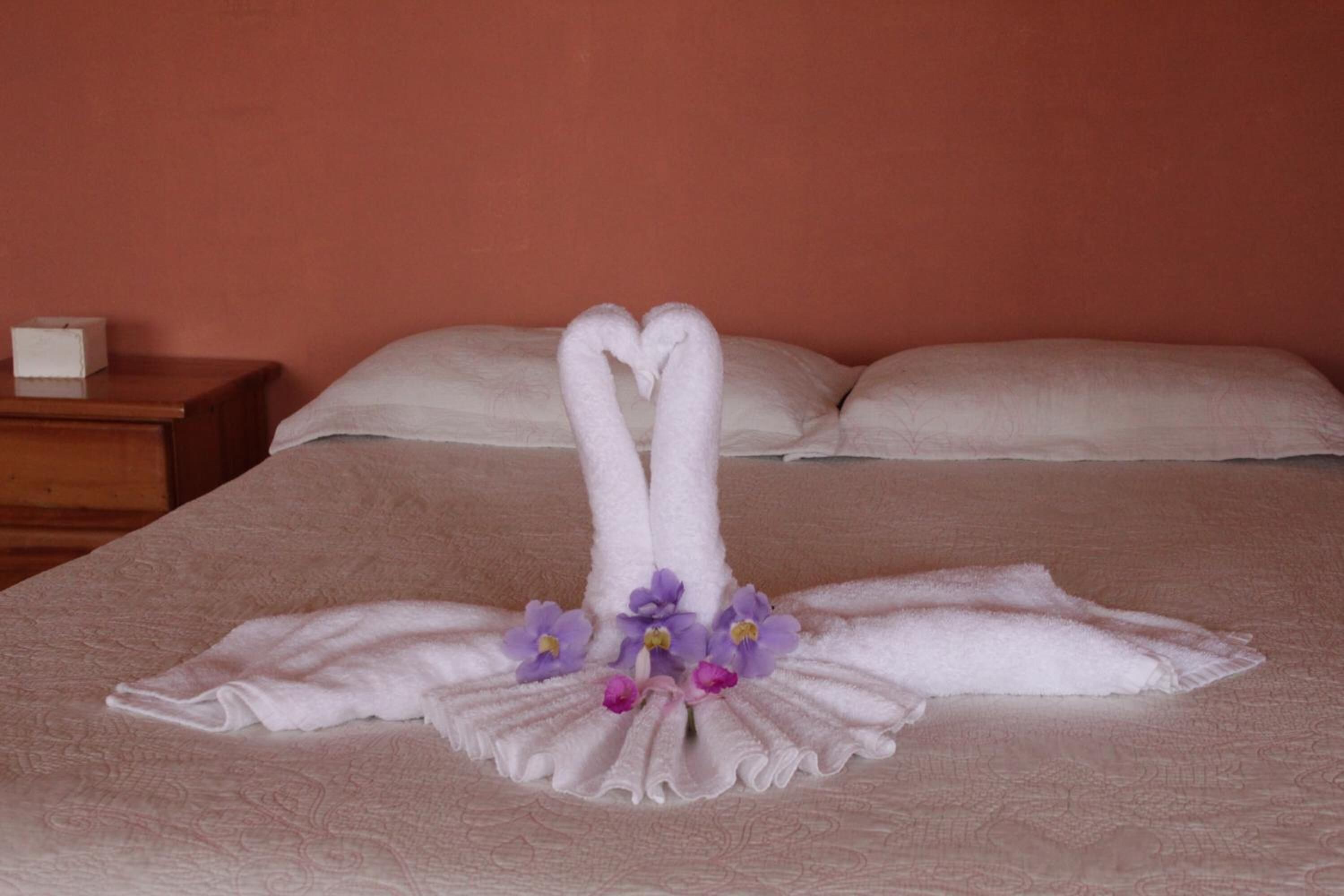 A bed with a towel arrangement in the shape of swans and purple flowers.
