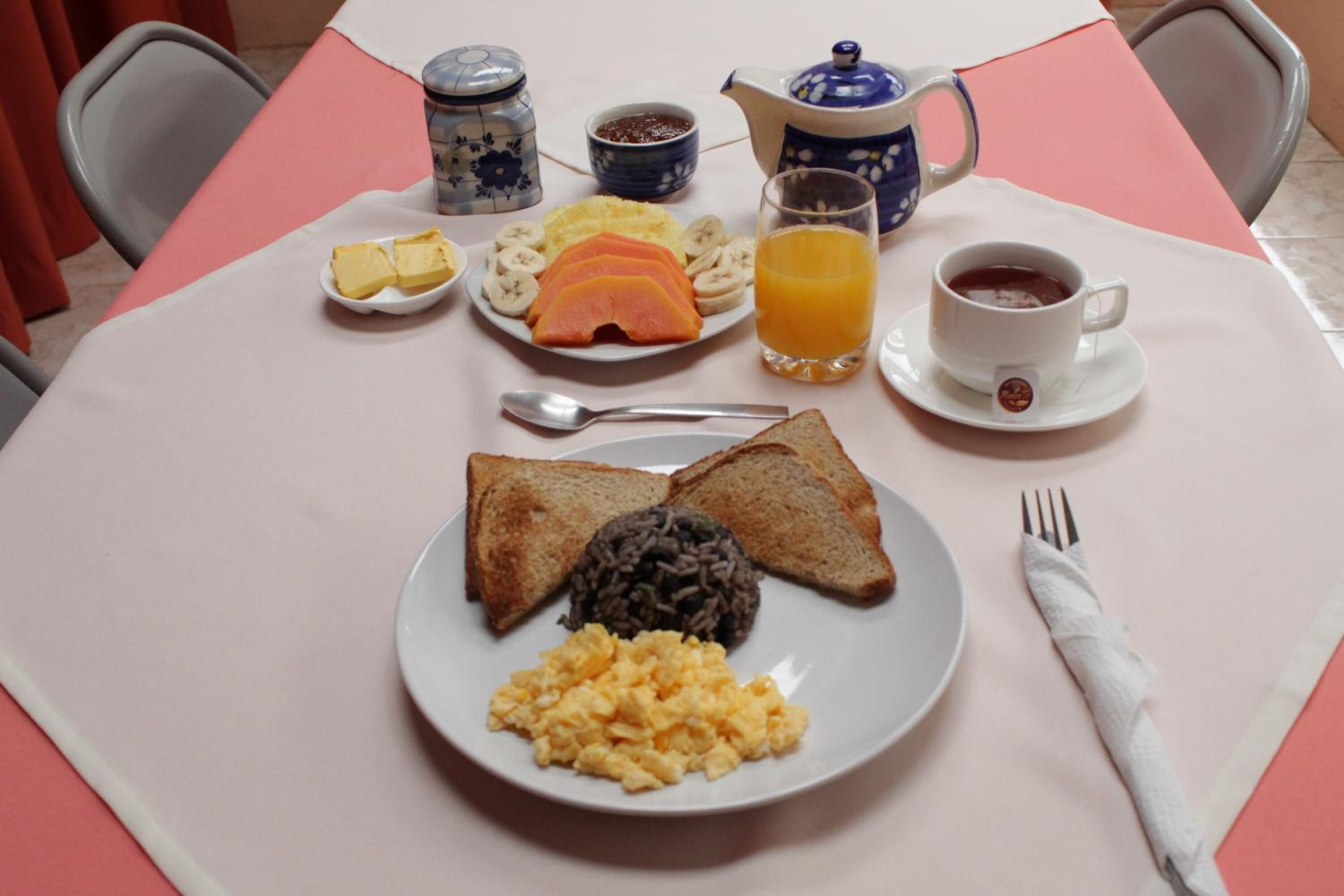 A breakfast table with toast, scrambled eggs, black pudding, ham, bananas, and orange juice.