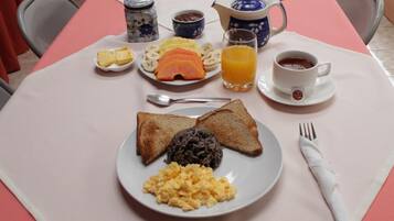 A breakfast table with toast, scrambled eggs, black pudding, ham, bananas, and orange juice.