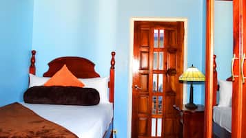 Un dormitorio con una cama de madera, una mesita de noche con lámpara y una puerta que da a otra habitación.