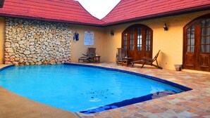 Una piscina con paredes de piedra y techos rojos, rodeada de puertas y sillas de madera.