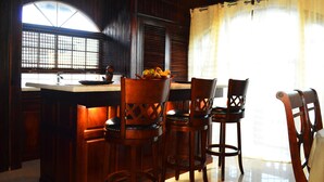 Una cocina con taburetes de madera, un frutero y una ventana con diseño de cuadrícula.
