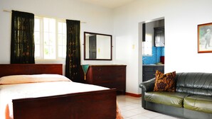 A bedroom with a bed, a dresser, a mirror, a sofa, and a kitchen area visible through an open door. - On Top of The Bay (Montego Bay)