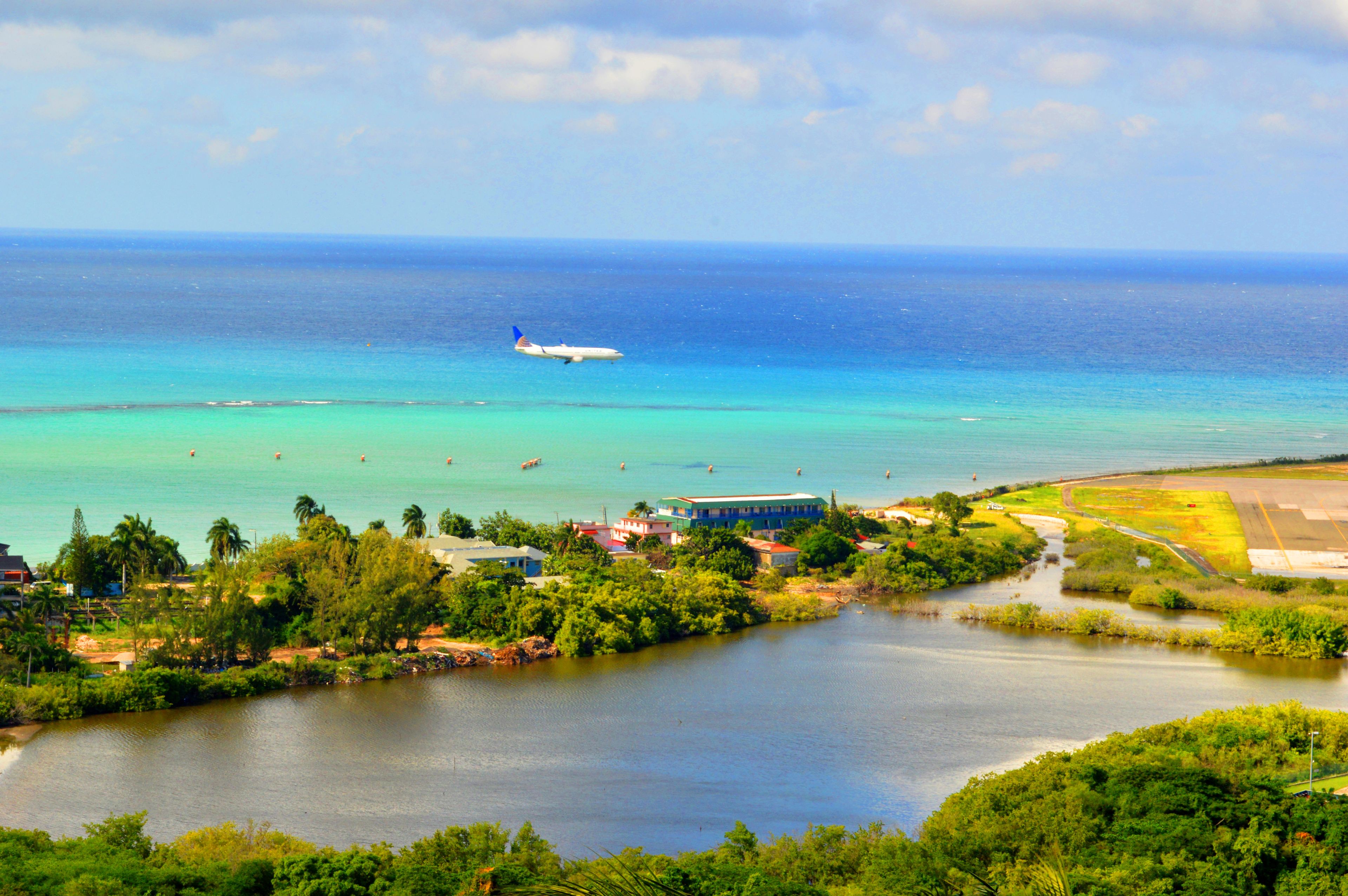 A coastal area with a clear view of the ocean, a river, and a small airport with an airplane.