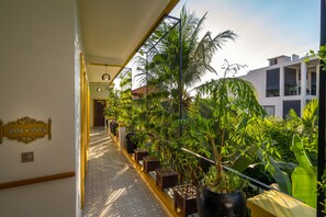 A corridor with potted plants, a sign with numbers, and a building in the background. - Beyond Yangon Boutique Inn (Siem Reap)