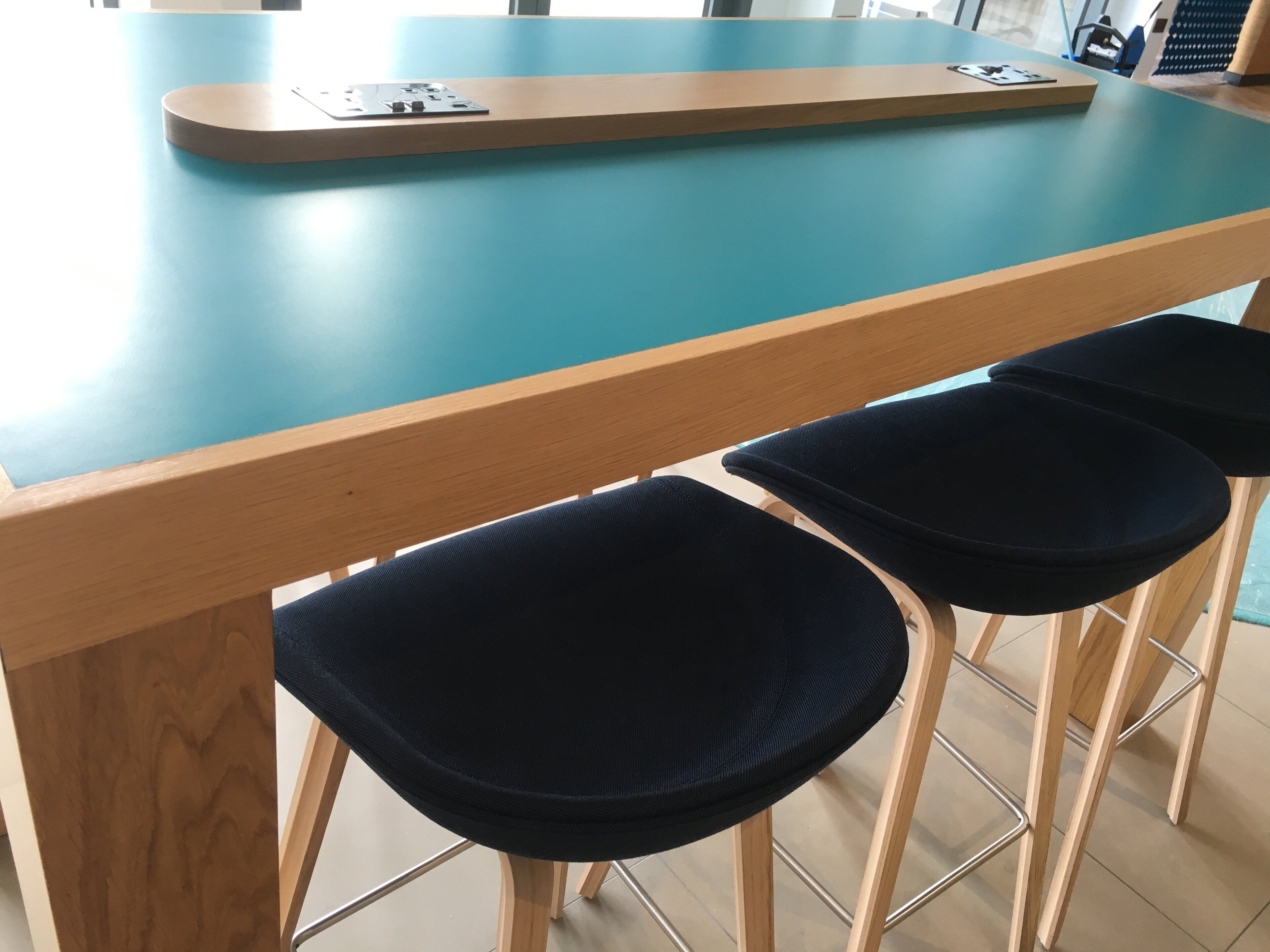 A wooden table with a blue top and metal legs, accompanied by dark blue upholstered chairs.