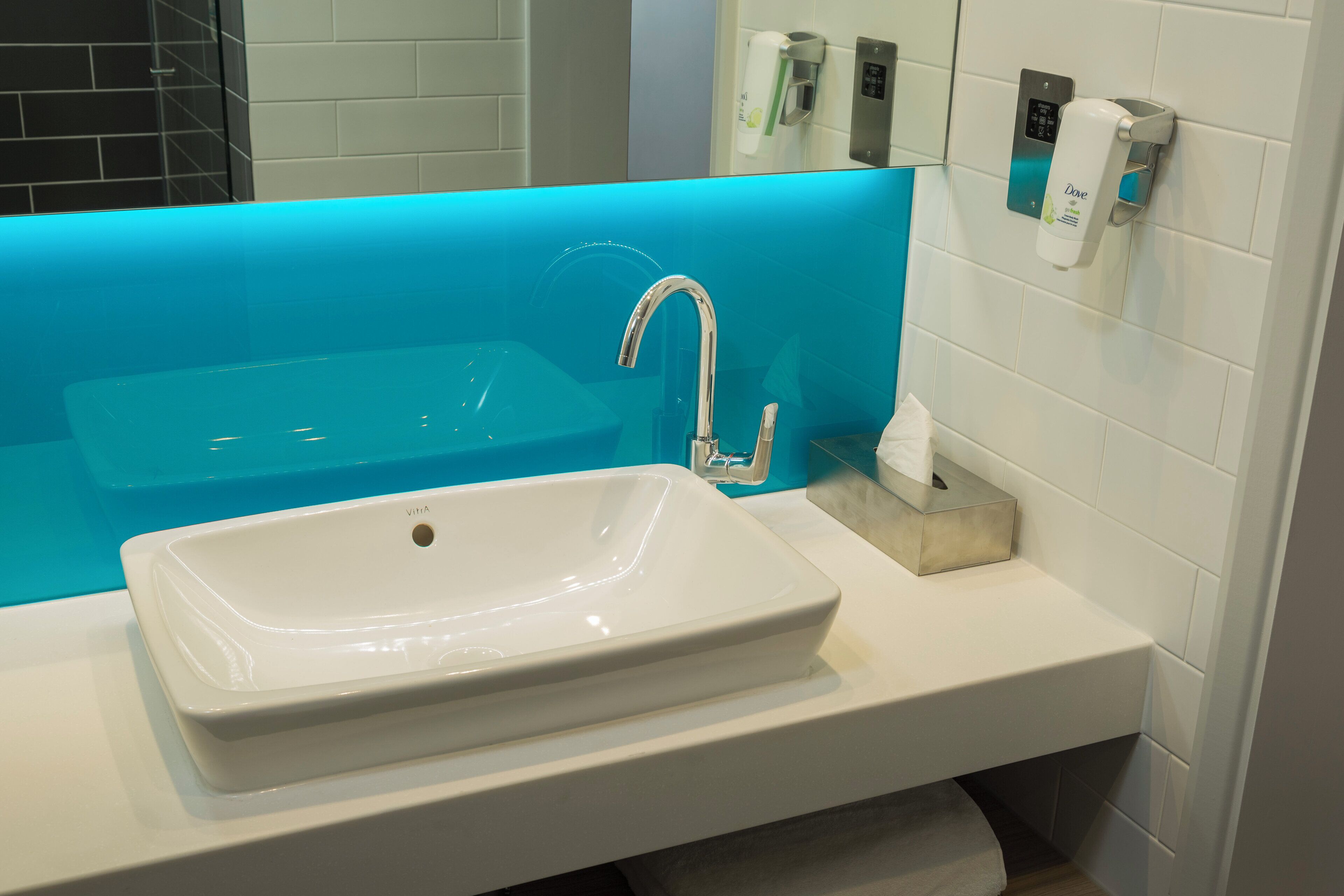 A bathroom with a white sink, a blue accent wall, and a hand dryer.