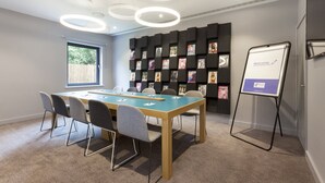 A conference room with a long table, chairs, a whiteboard, and a bookshelf with magazines. - Holiday Inn Express St. Albans - M25, Jct.22 by IHG (St Albans)
