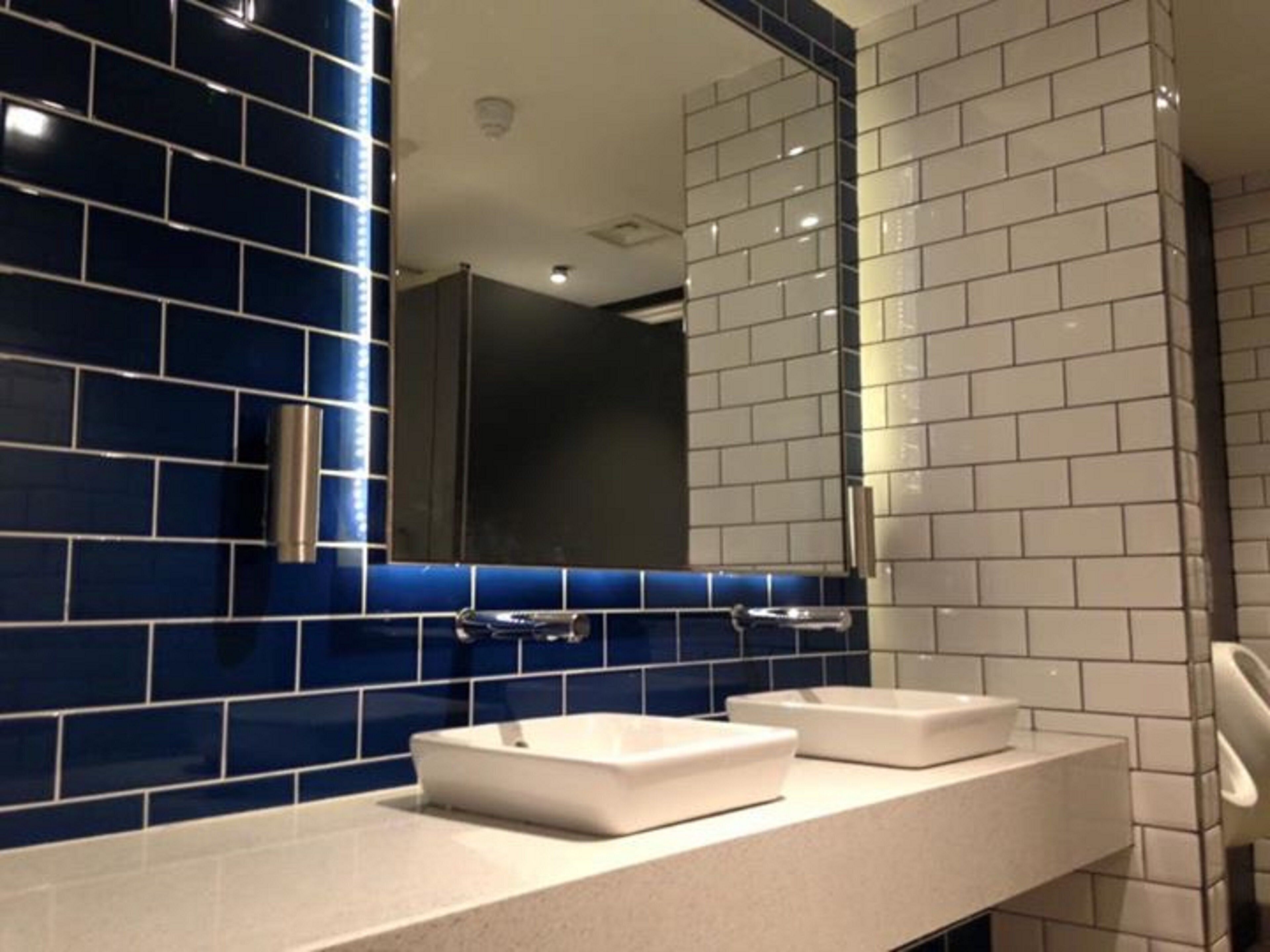 Een badkamer met blauw-witte betegelde muren, twee wastafels en een spiegel.