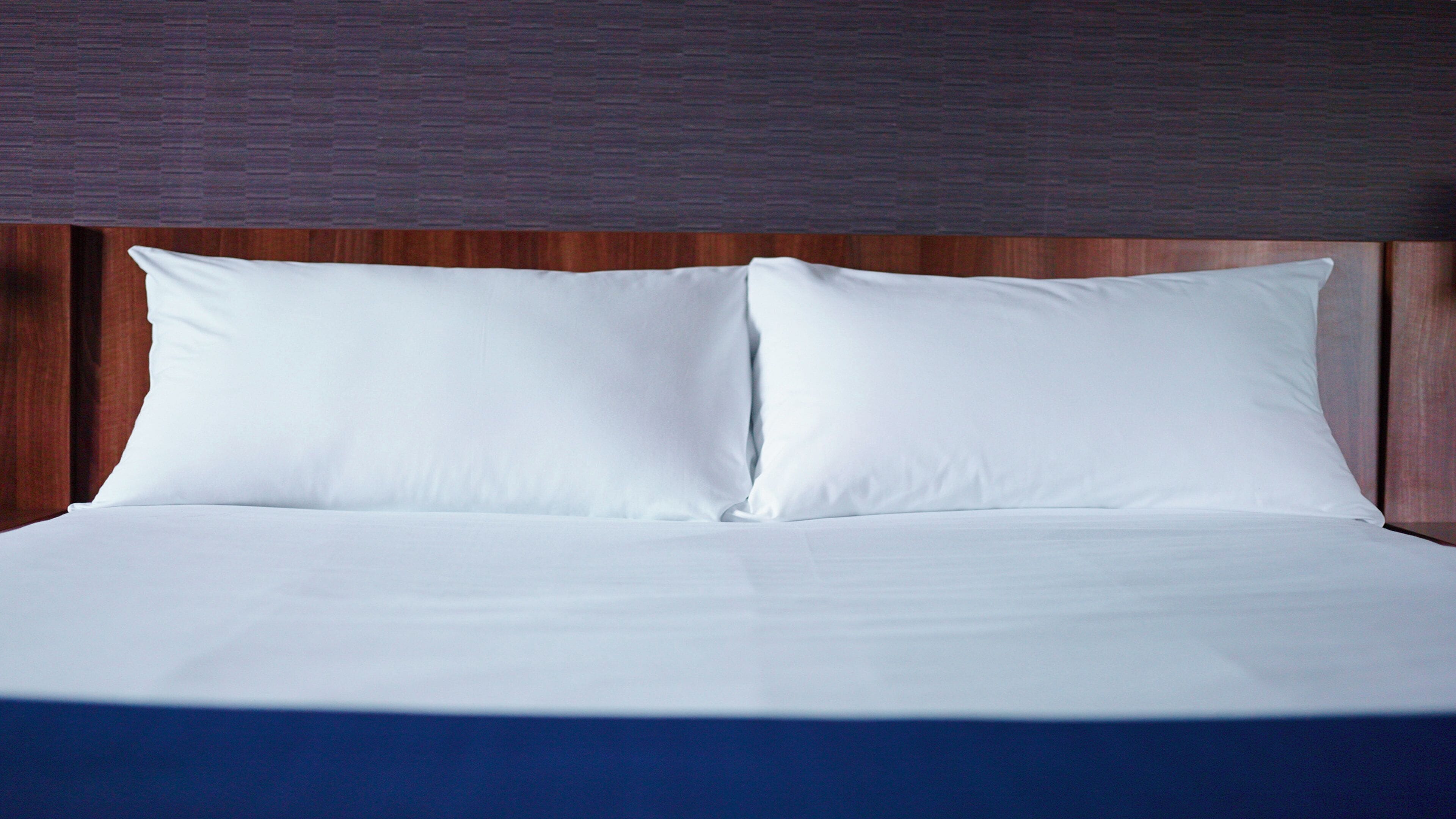 Una cama bien tendida con sábanas blancas y un cabecero de madera.