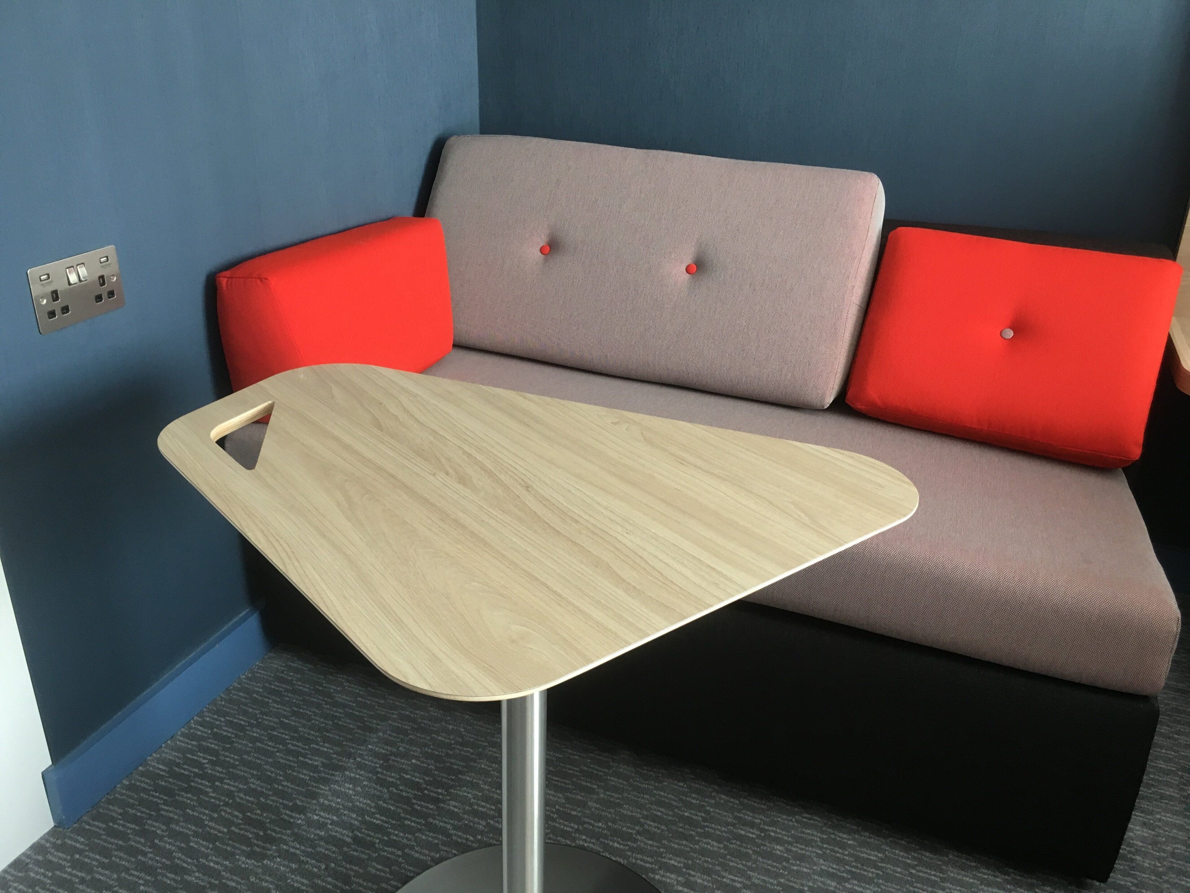 Una habitación moderna con un sofá gris, cojines rojos y una mesa de madera con una asa recortada.