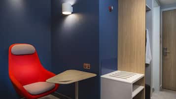 A modern hotel room with a red chair, a small table, and a built-in wardrobe.