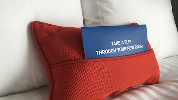 A red pillow with a blue card on a bed with white and striped bedding.