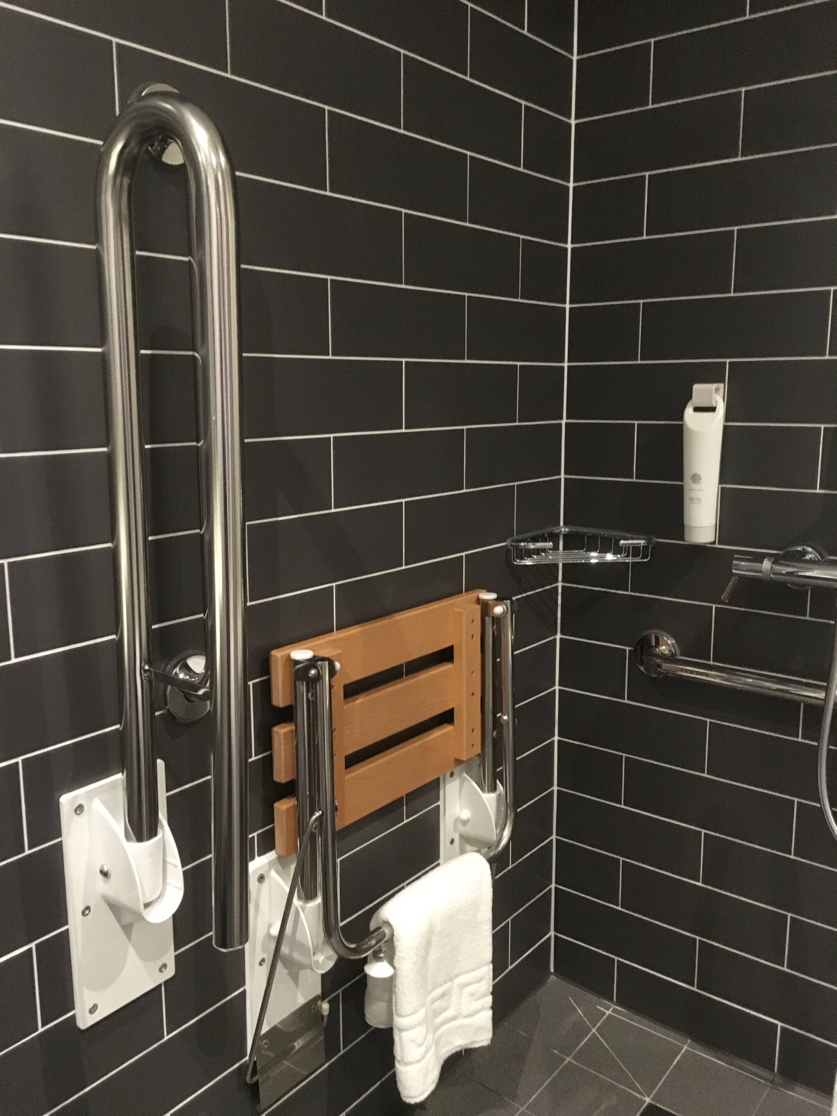 Ett badrum med svarta kakelväggar, ett trähandduksställ, en vit handduk och en tvålpump.
