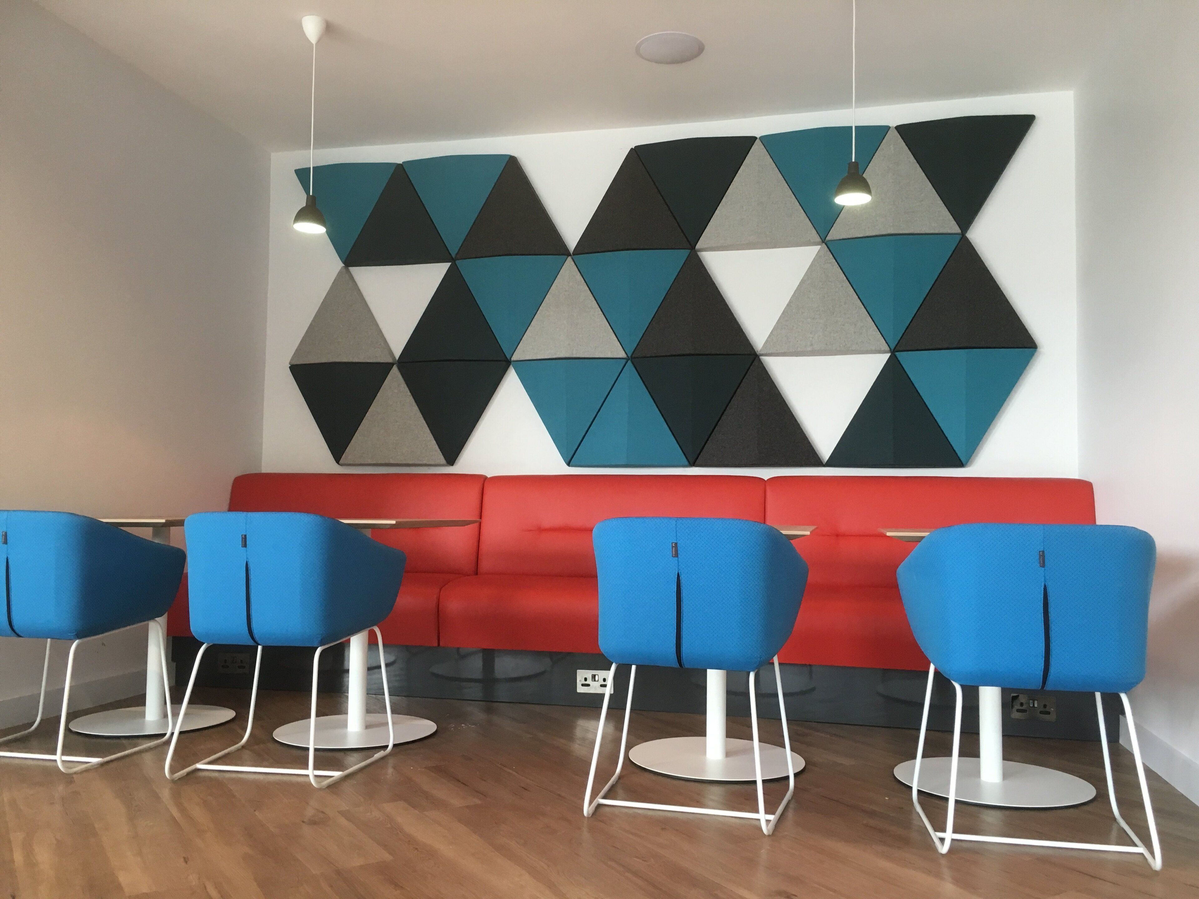 Um interior moderno com sofá vermelho e cadeiras azuis, arte geométrica nas paredes e iluminação pendente.