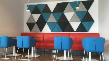 Um interior moderno com sofá vermelho e cadeiras azuis, arte geométrica nas paredes e iluminação pendente.