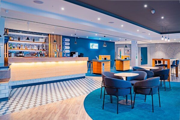 Un hall d’hôtel moderne doté d’un bar, de coins salon et d’un comptoir d’enregistrement.