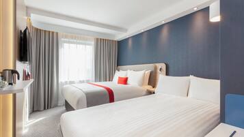 A hotel room with two beds, a TV, a desk, and a window with curtains.