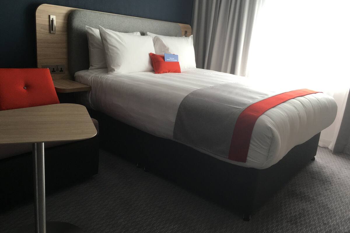 A hotel room with a bed, a nightstand, a desk, and a window with curtains.