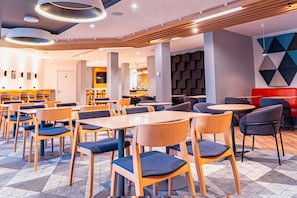 A modern dining area with wooden tables and chairs, a patterned floor, and a geometric wall design.