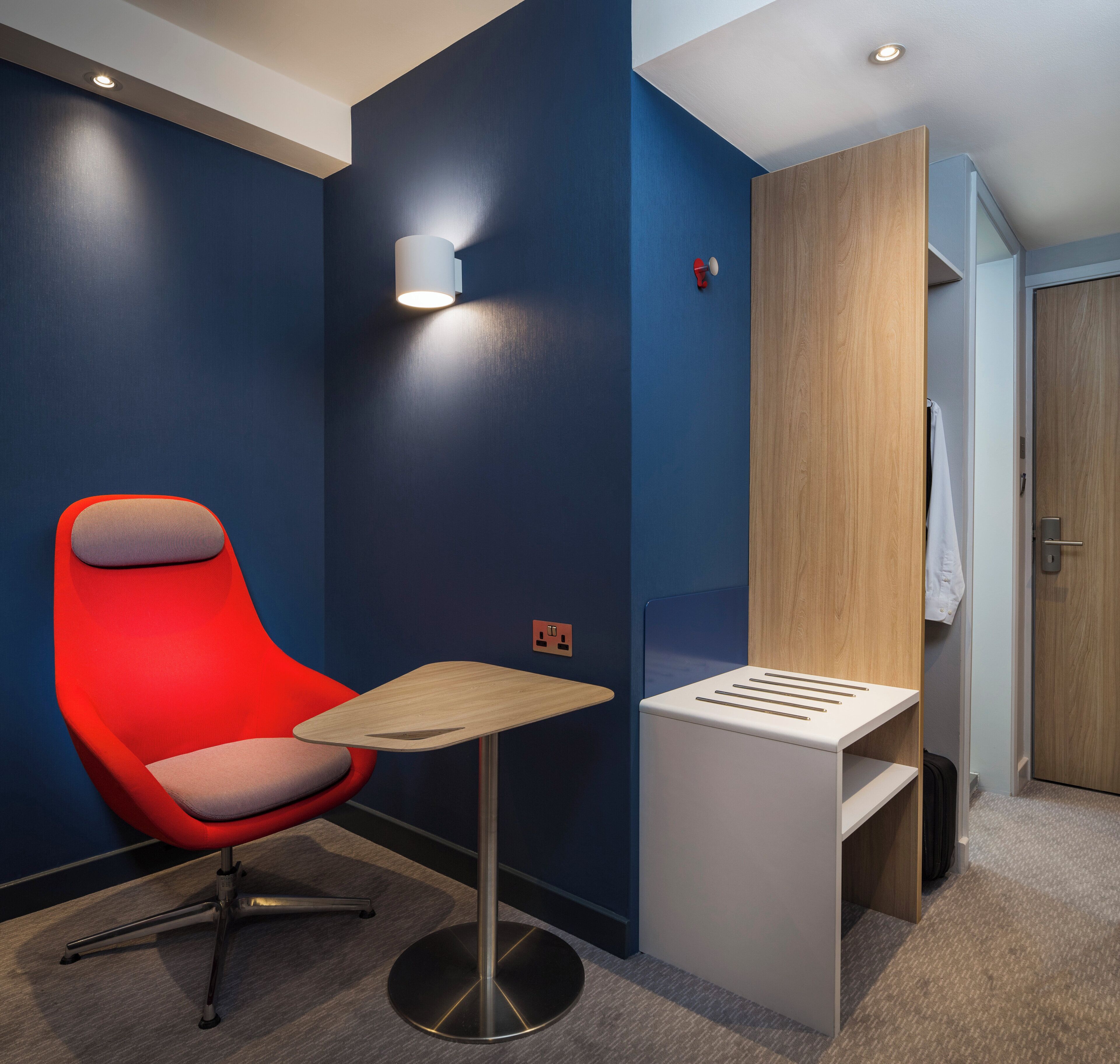 Una habitación moderna con una silla roja, una mesita pequeña y un armario de madera.