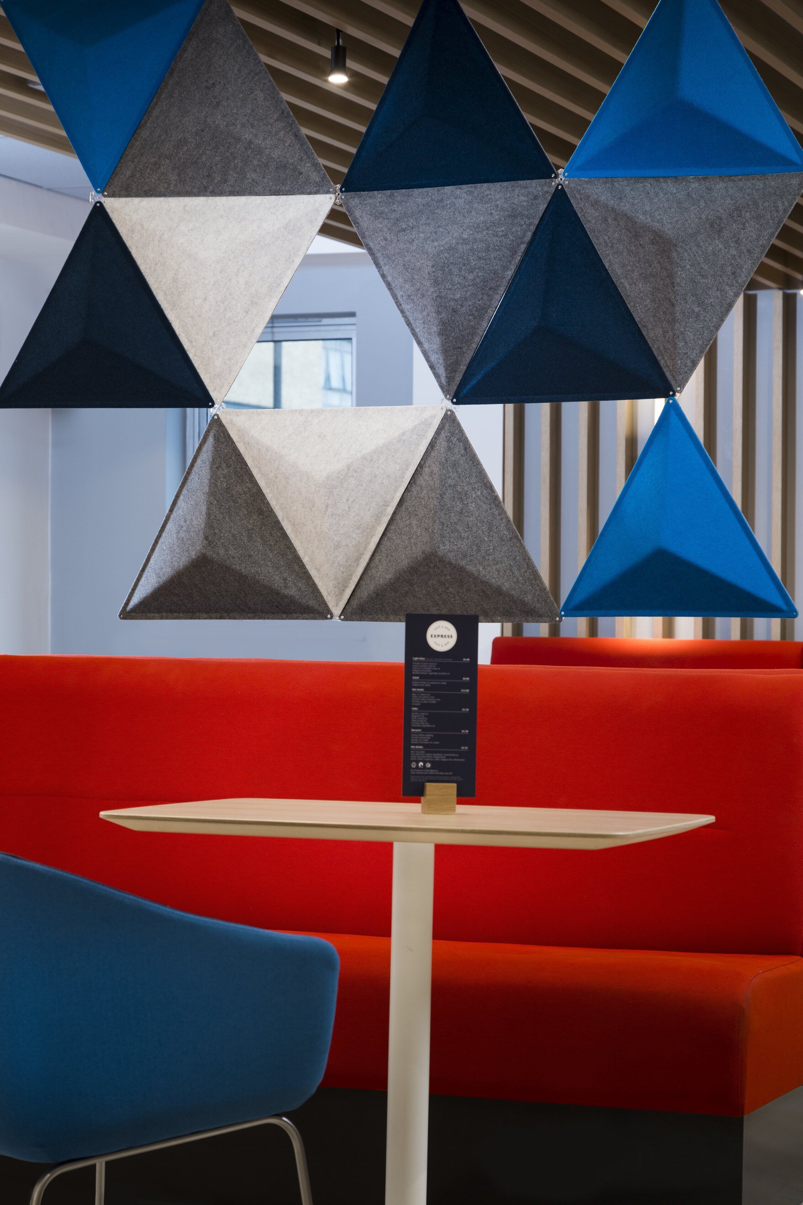 A modern interior with a red couch, a blue chair, and a table with a menu.