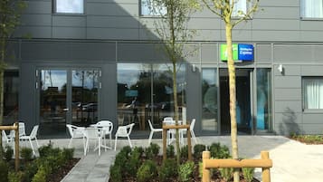 Un edificio moderno con un letrero de Holiday Inn Express, zona de estar al aire libre con sillas blancas y un jardín bien cuidado.