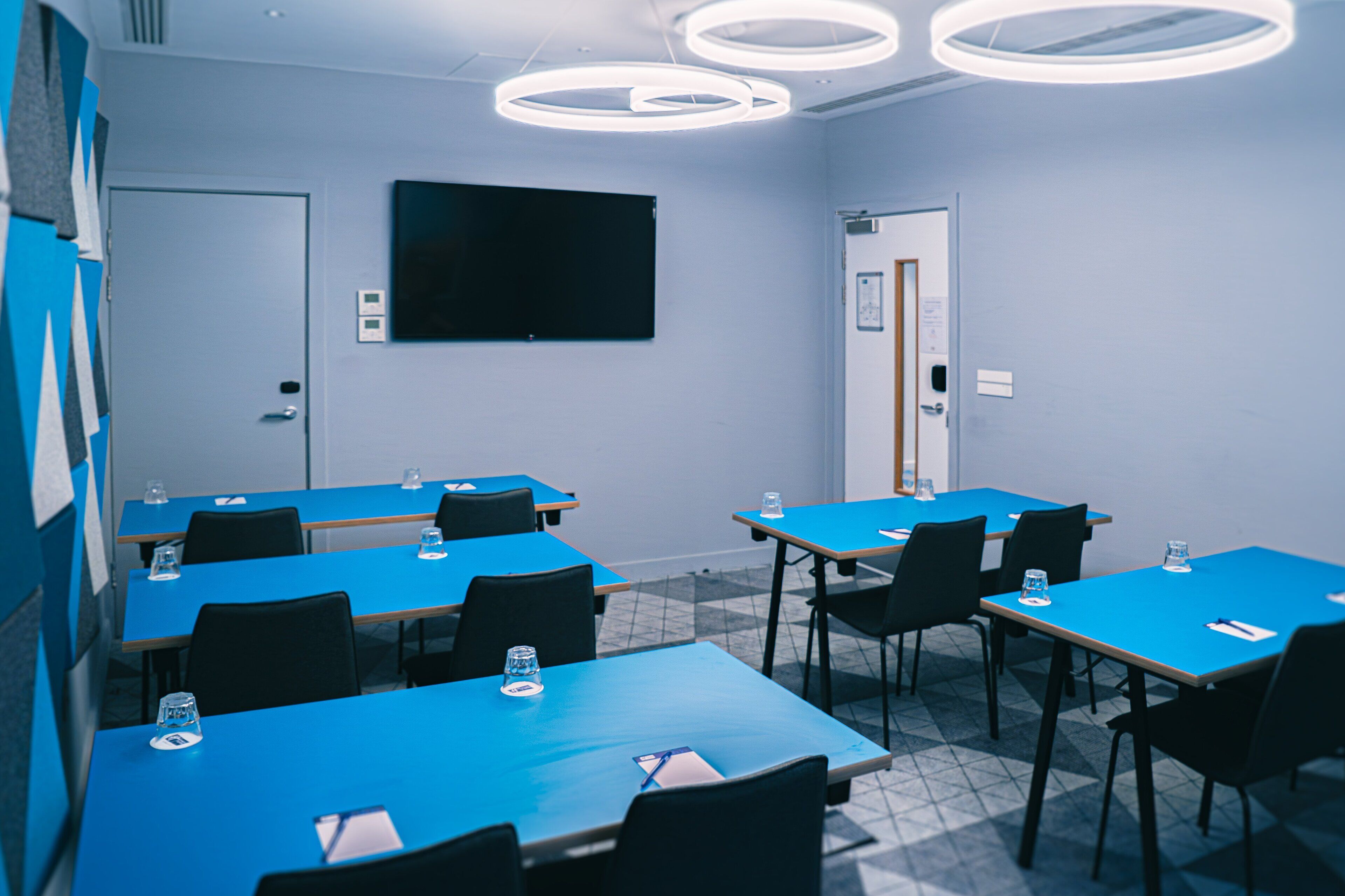 A conference room with blue tables and chairs, a blackboard, and circular ceiling lights.