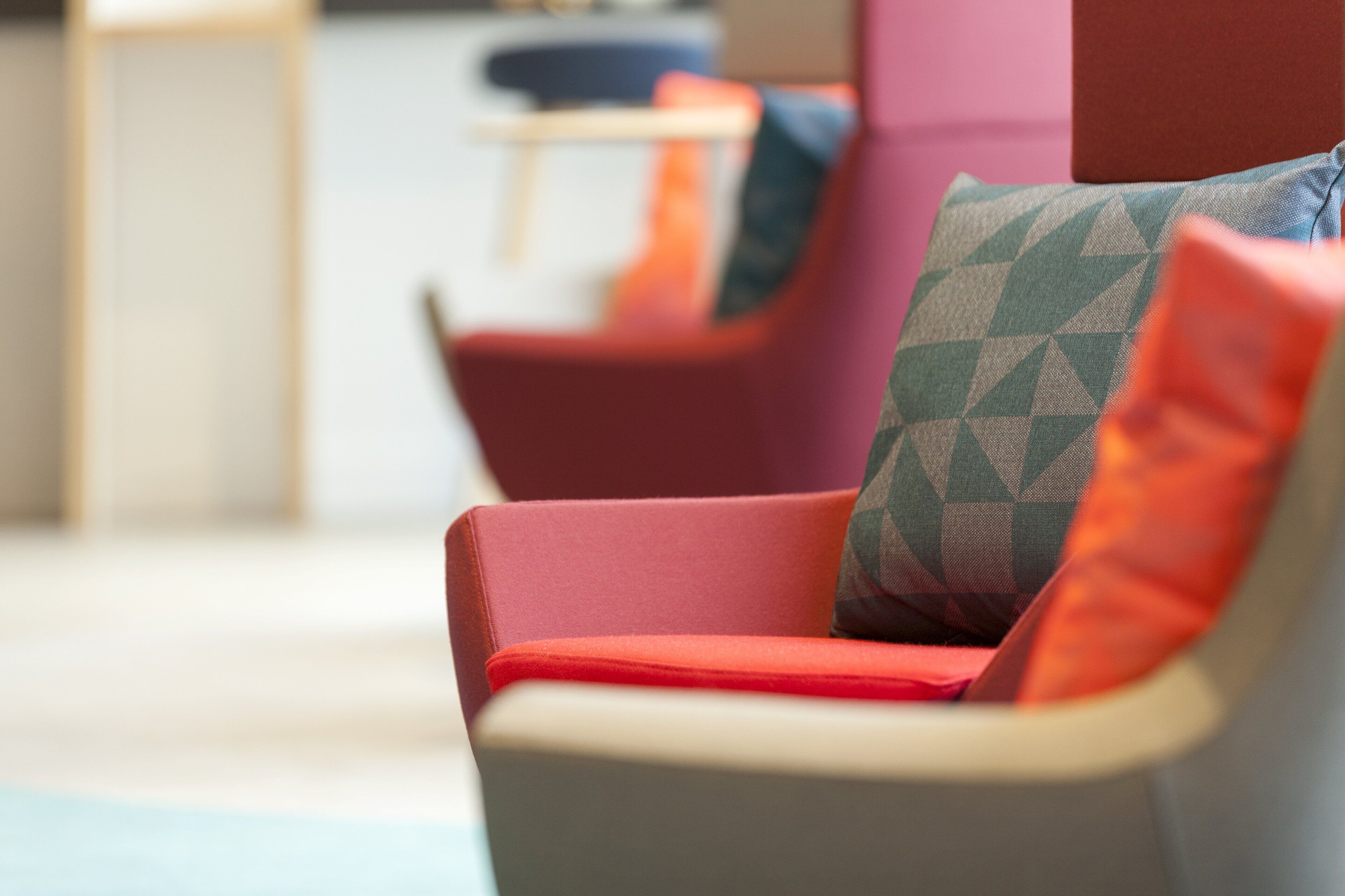A modern lounge area with a red and grey armchair, a patterned cushion, and a blue and orange chair in the background.