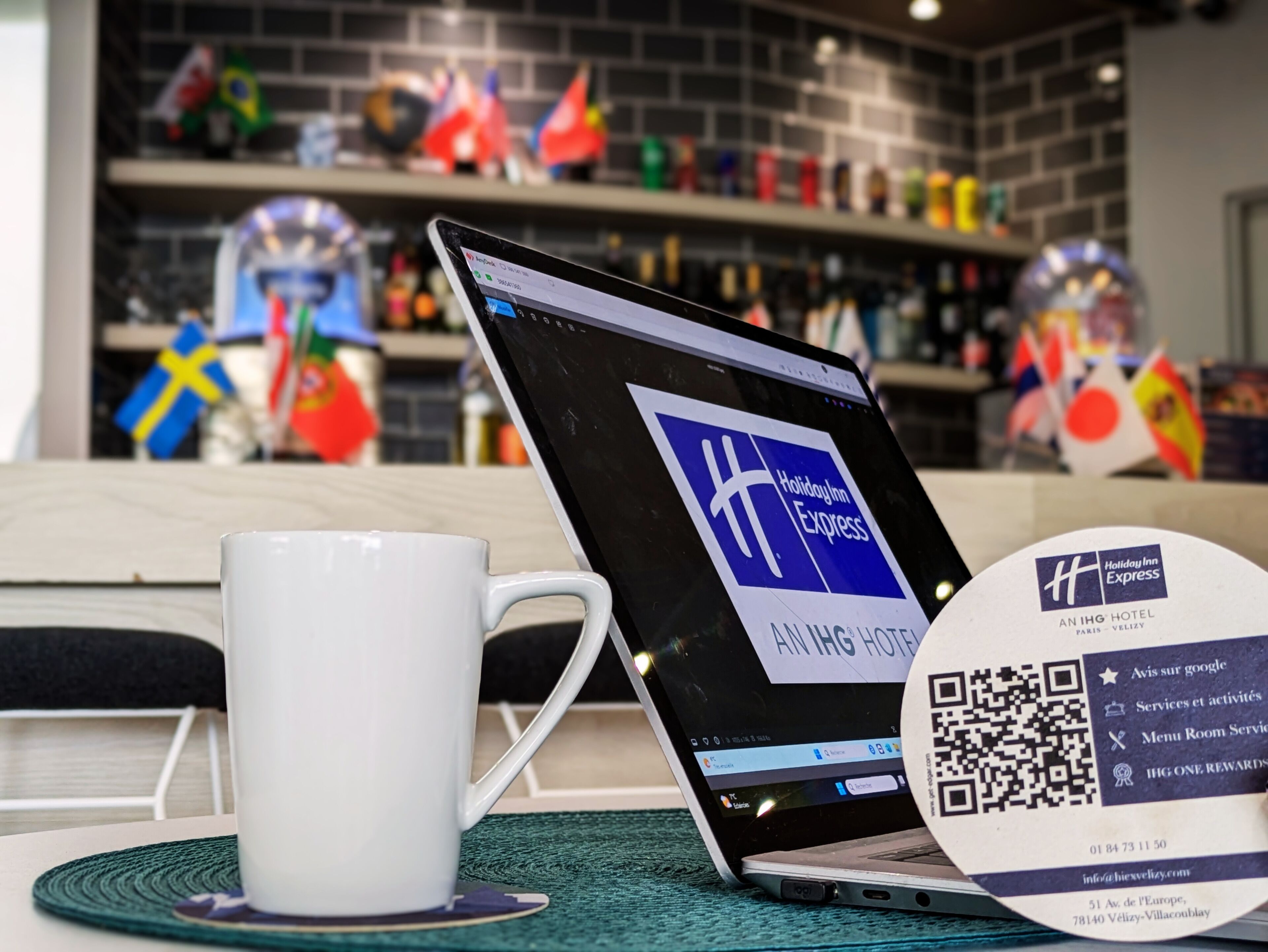 Una computadora portátil mostrando la página web de Holiday Inn Express, una taza blanca y un código QR sobre un posavasos.