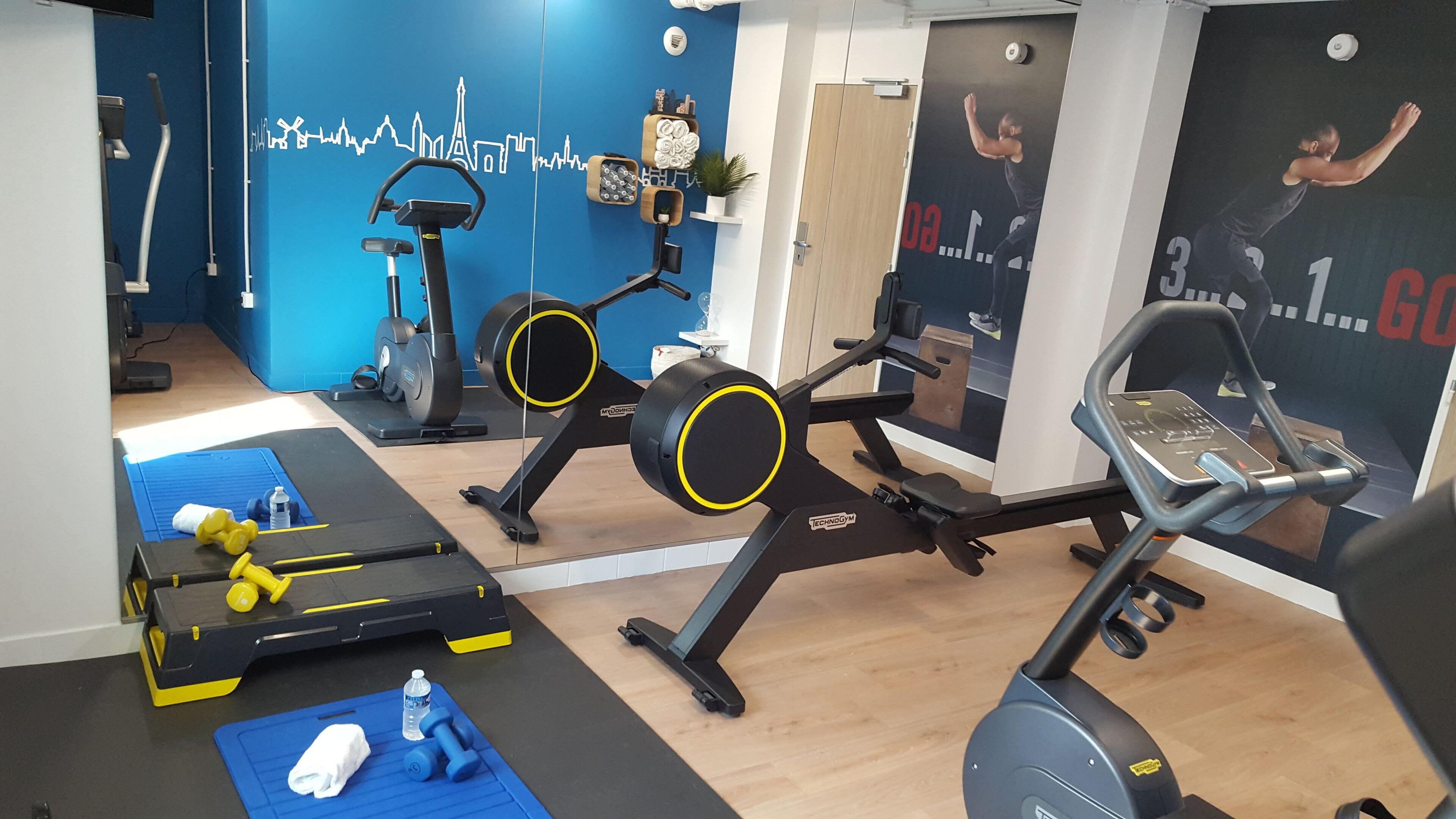 A gym with cardio machines, dumbbells, and a blue mat.