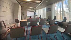 Une salle de conférence au design moderne, dotée d’un grand écran, de nombreuses chaises et offrant une vue sur l’extérieur grâce à de grandes fenêtres.