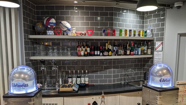 Uma área de bar com prateleiras cheias de garrafas, copos e uma torneira de cerveja.