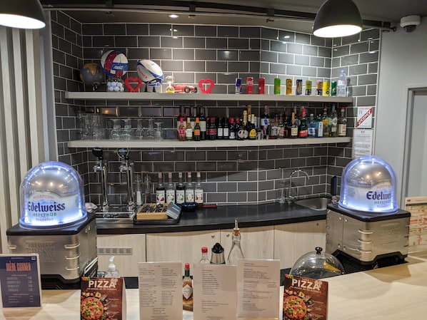 Una zona de bar con estantes llenos de botellas, vasos y una grifo de cerveza.