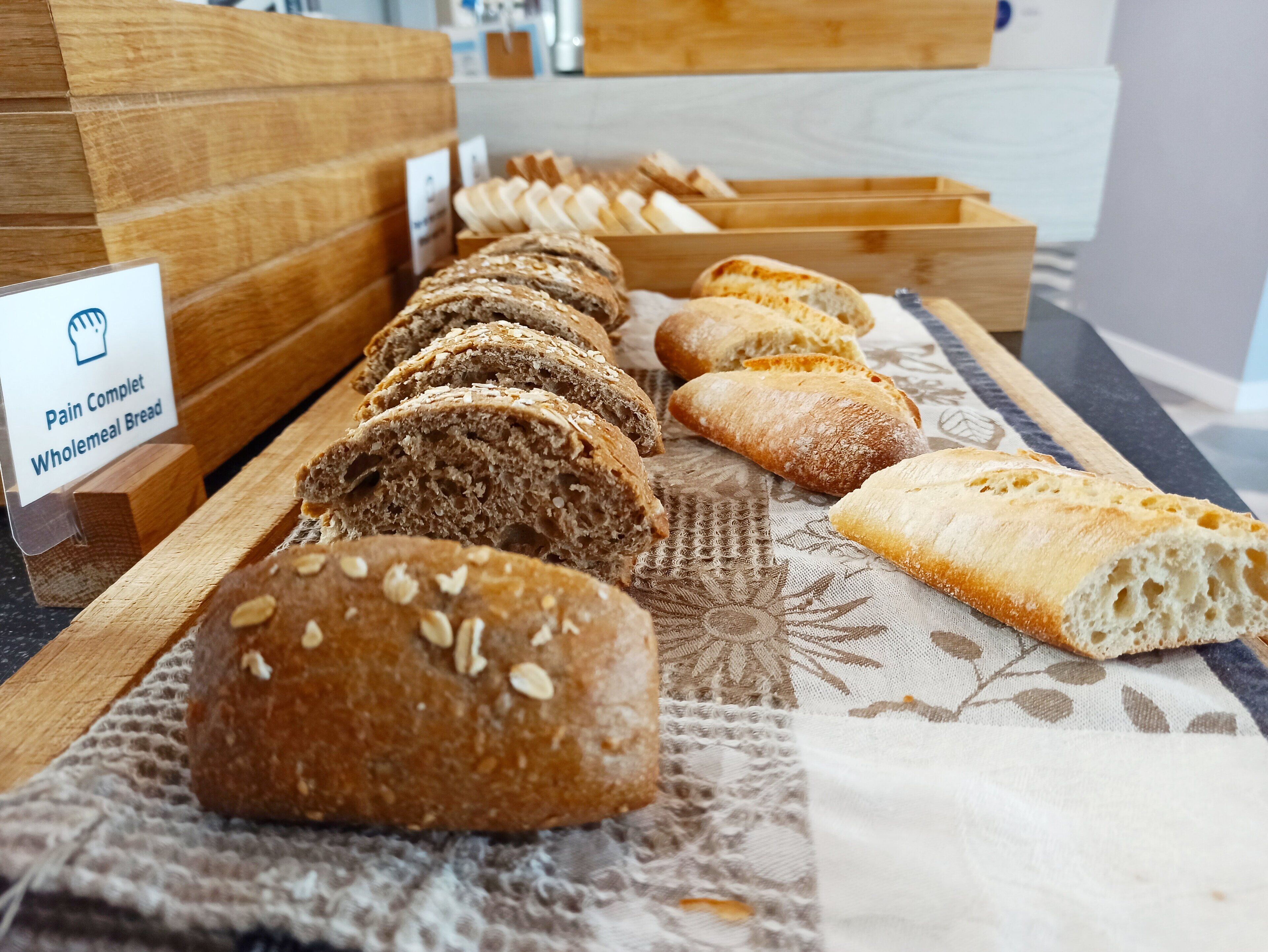 A variety of wholemeal breads displayed on a wooden counter with a label indicating "Pain Complet Wholemeal Bread".