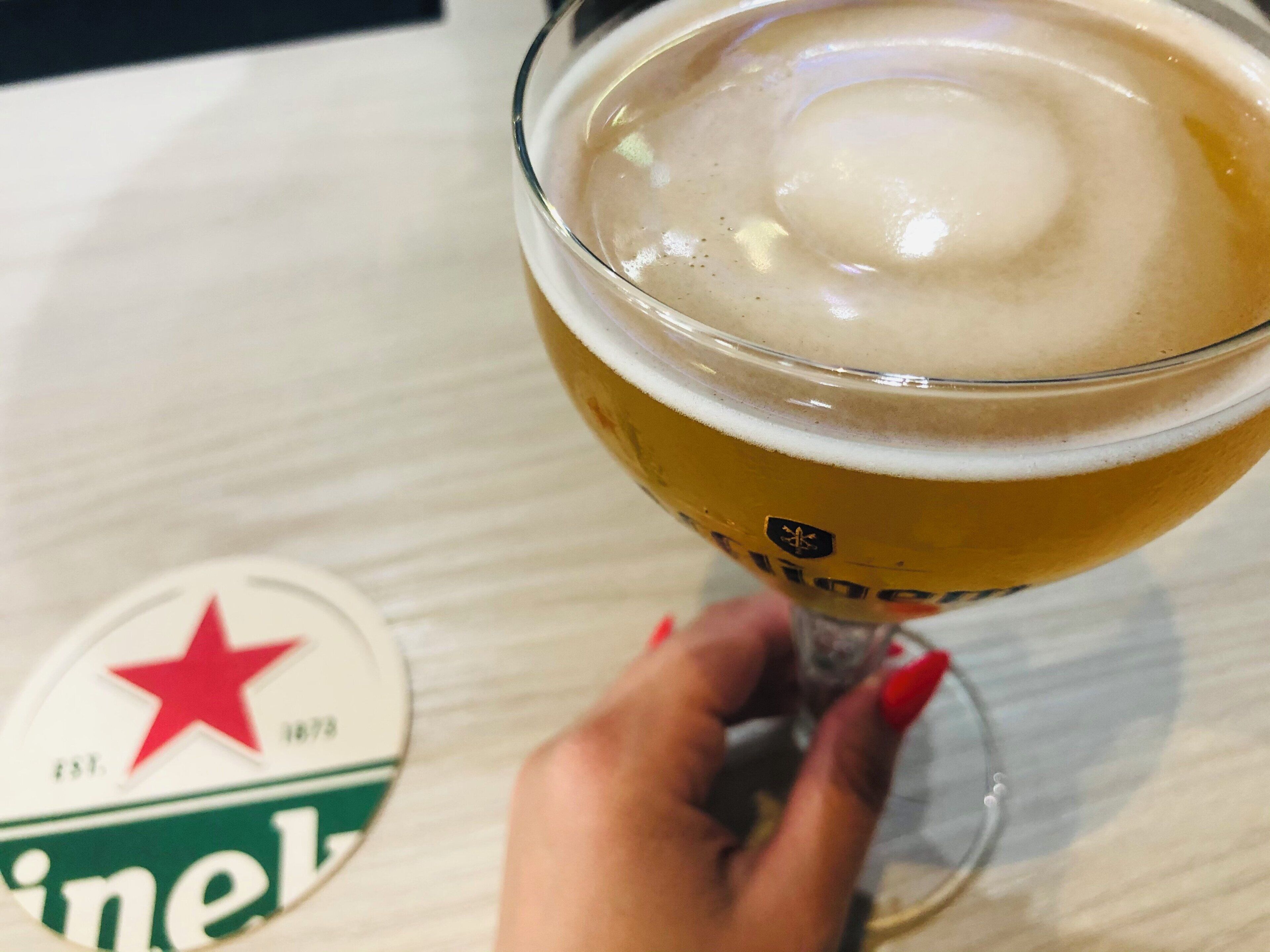 A hand holding a glass of beer with a logo on the glass, and a coaster with a logo on a table.