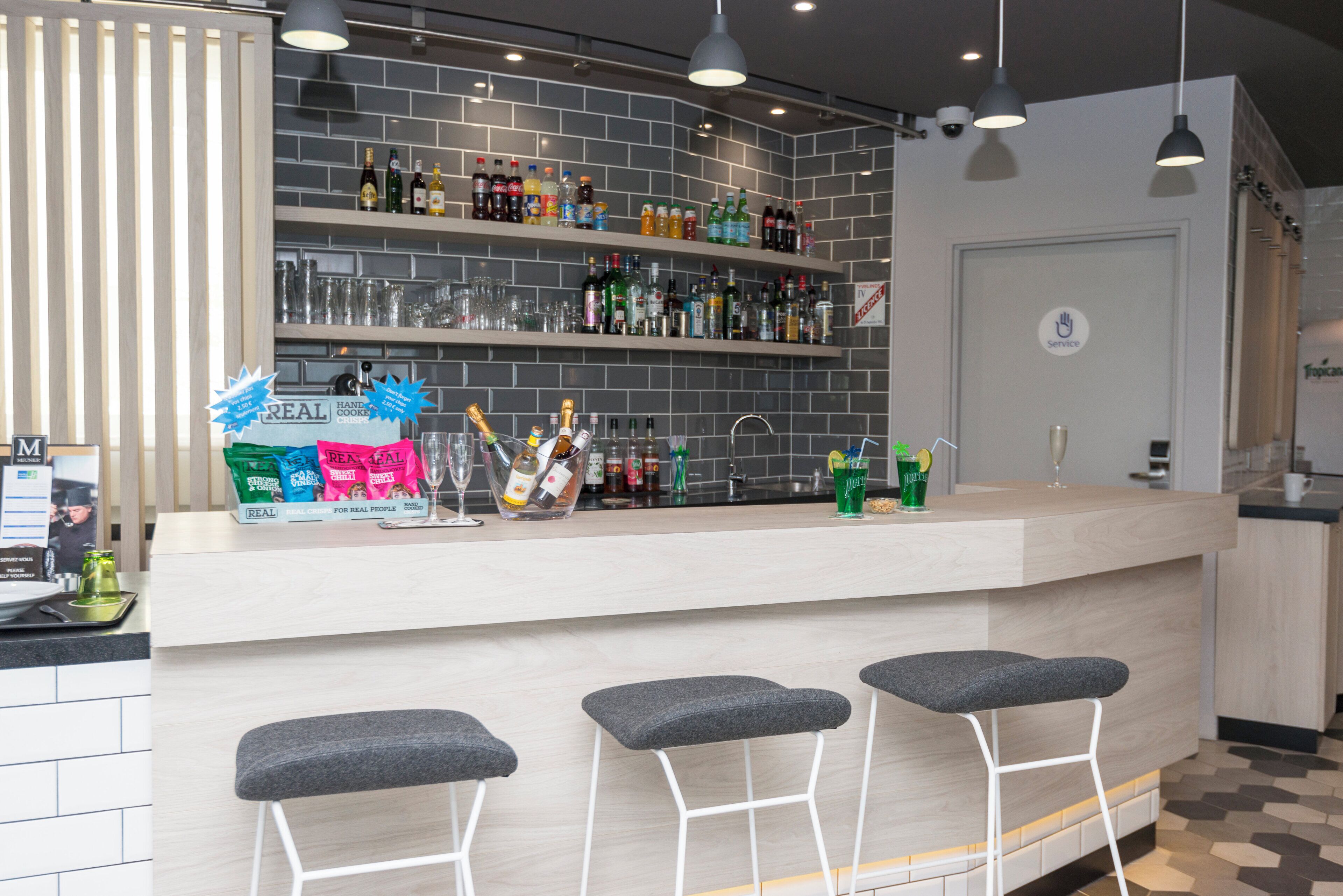 Angolo bar con un bancone, scaffali pieni di bevande e sgabelli da bar.