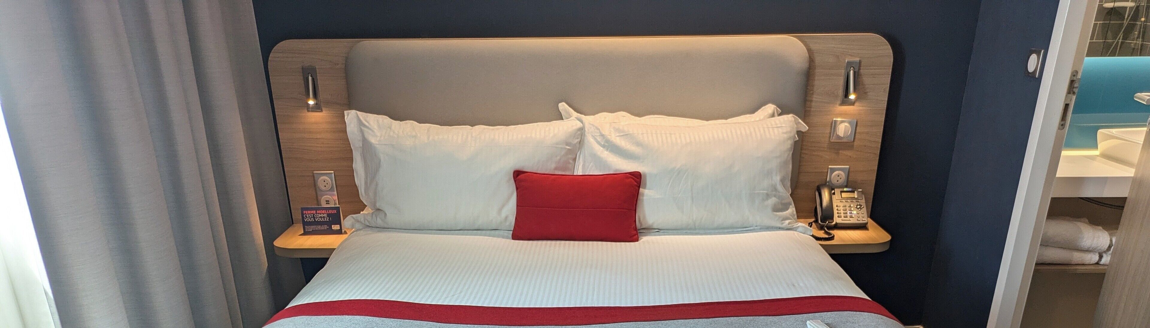 A hotel room with a bed, a red pillow, and a bedside telephone.