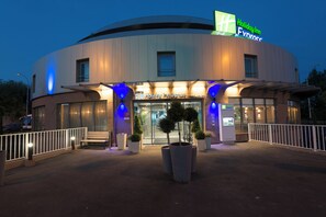 A Holiday Inn Express building with a curved facade, large entrance doors, and potted plants in front. - Holiday Inn Express Paris - Velizy by IHG (Velizy-Villacoublay)