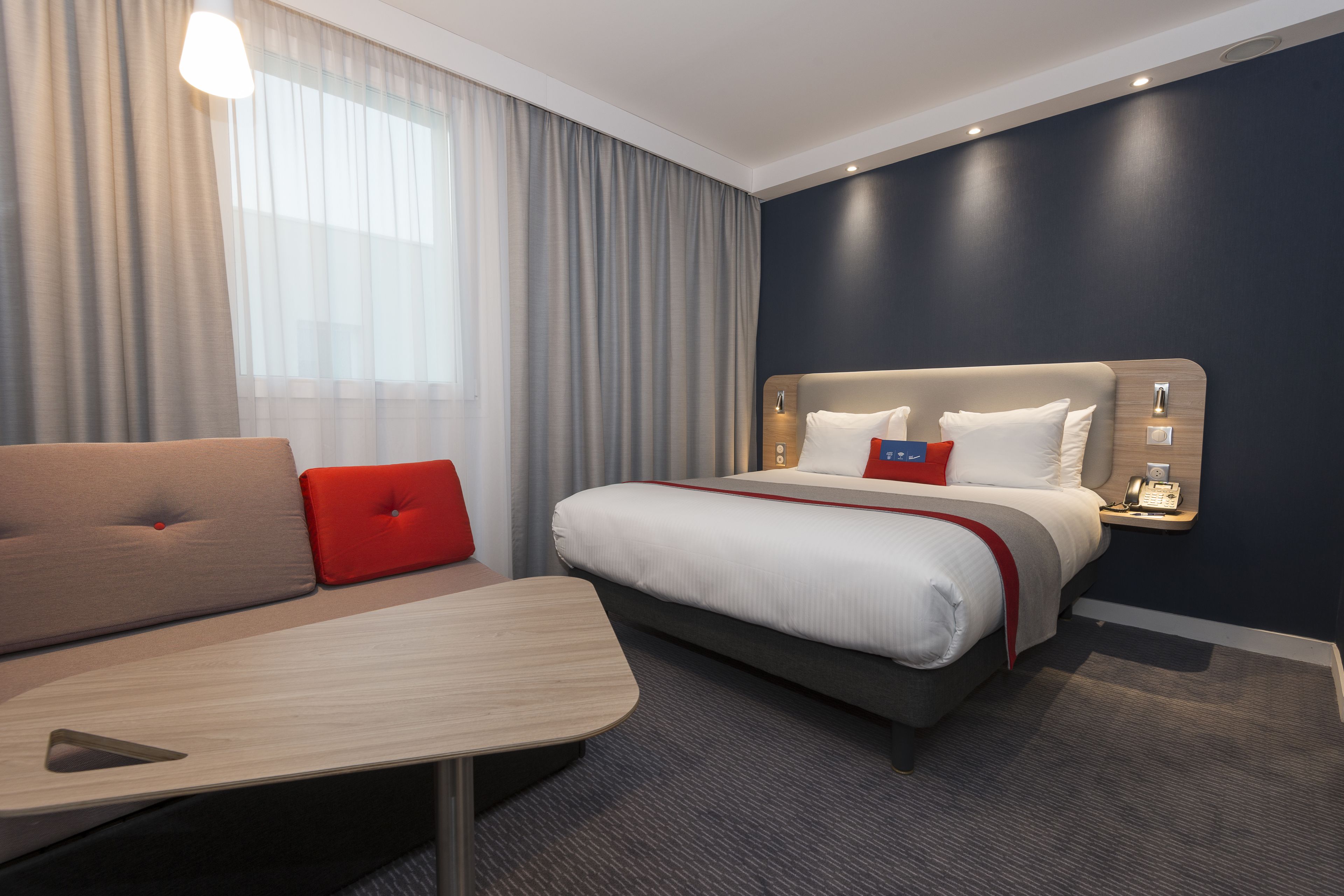 A hotel room with a bed, a sofa, a desk, and a telephone.