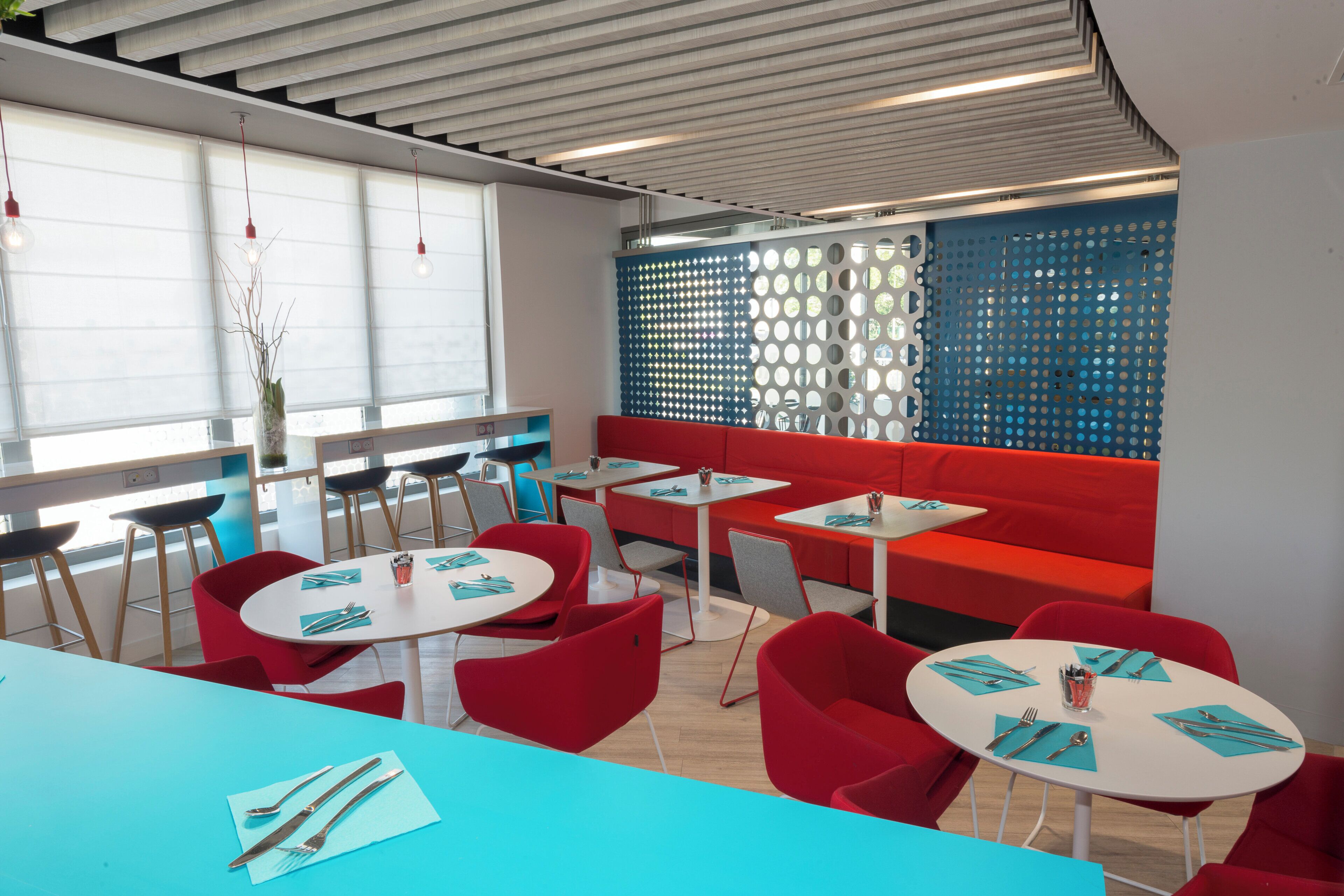 A modern dining area with round tables, red seating, and a decorative wall with circular cutouts.