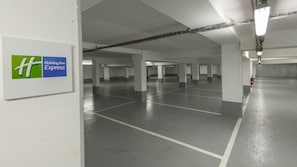 Un estacionamiento de Holiday Inn Express con múltiples espacios, pilares de hormigón e iluminación colgante.