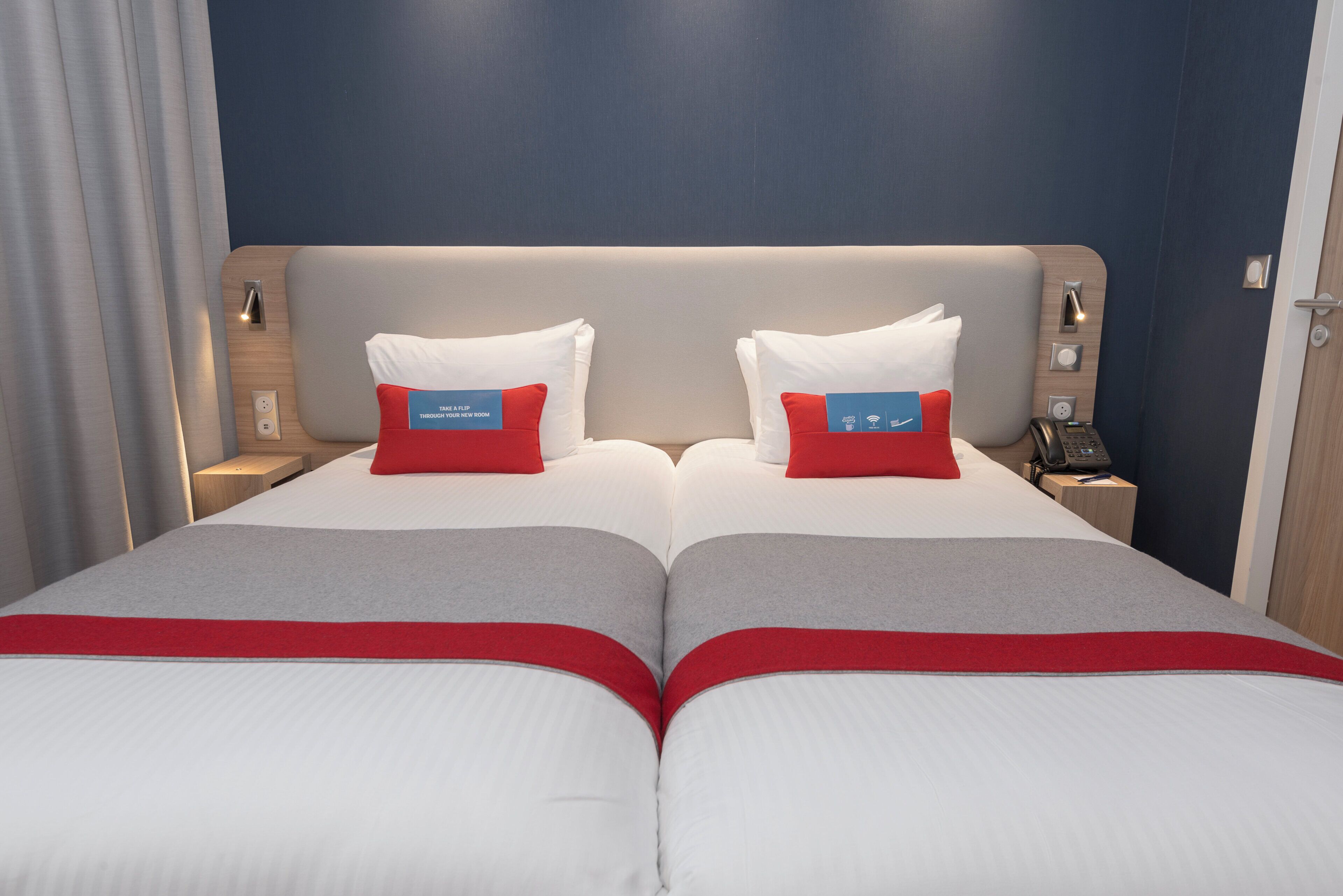 A double bed with a headboard, two bedside tables, a phone, and a nightstand with a lamp.