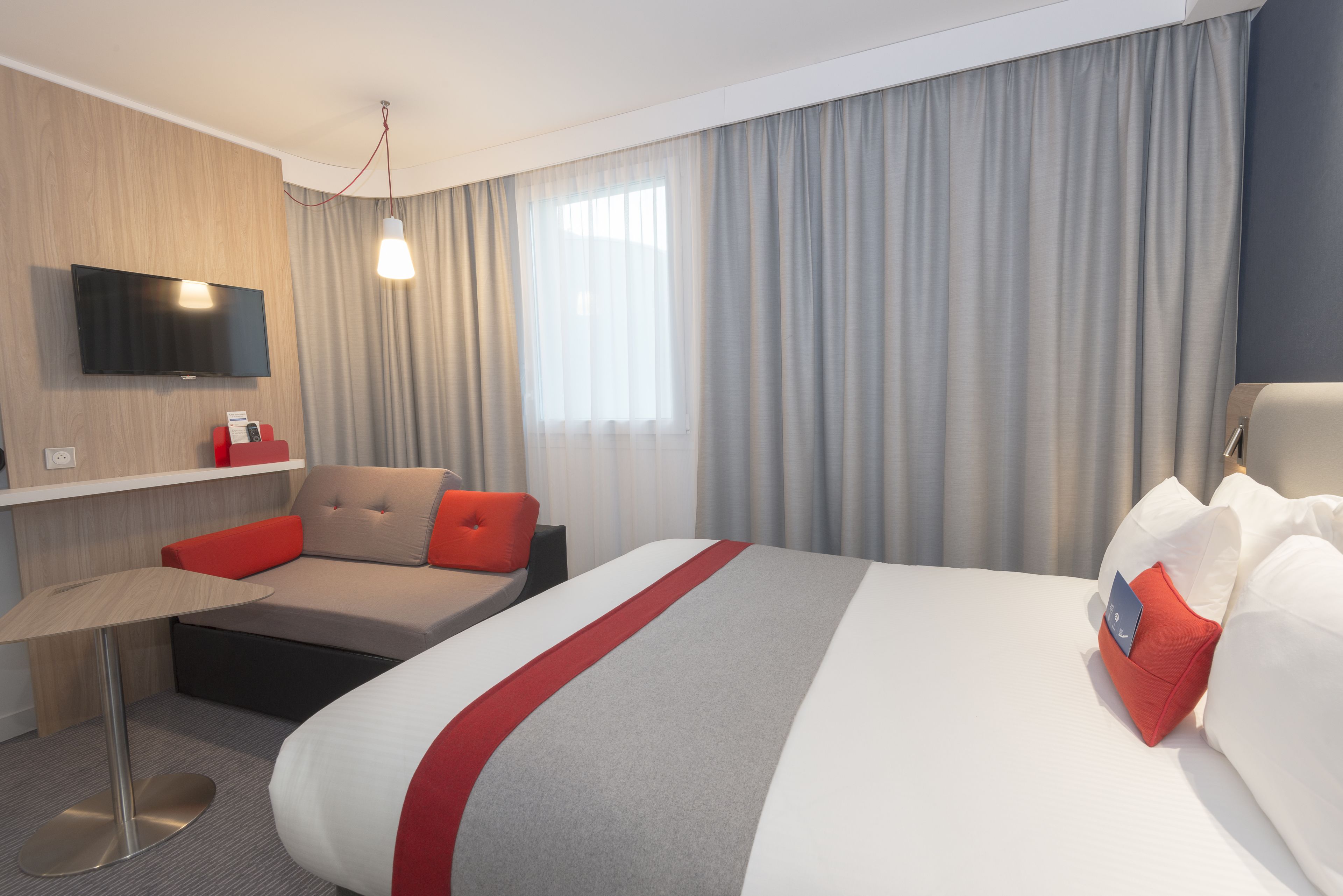 Hotelkamer met een bed, een bureau, een stoel, een televisie en een raam met gordijnen.