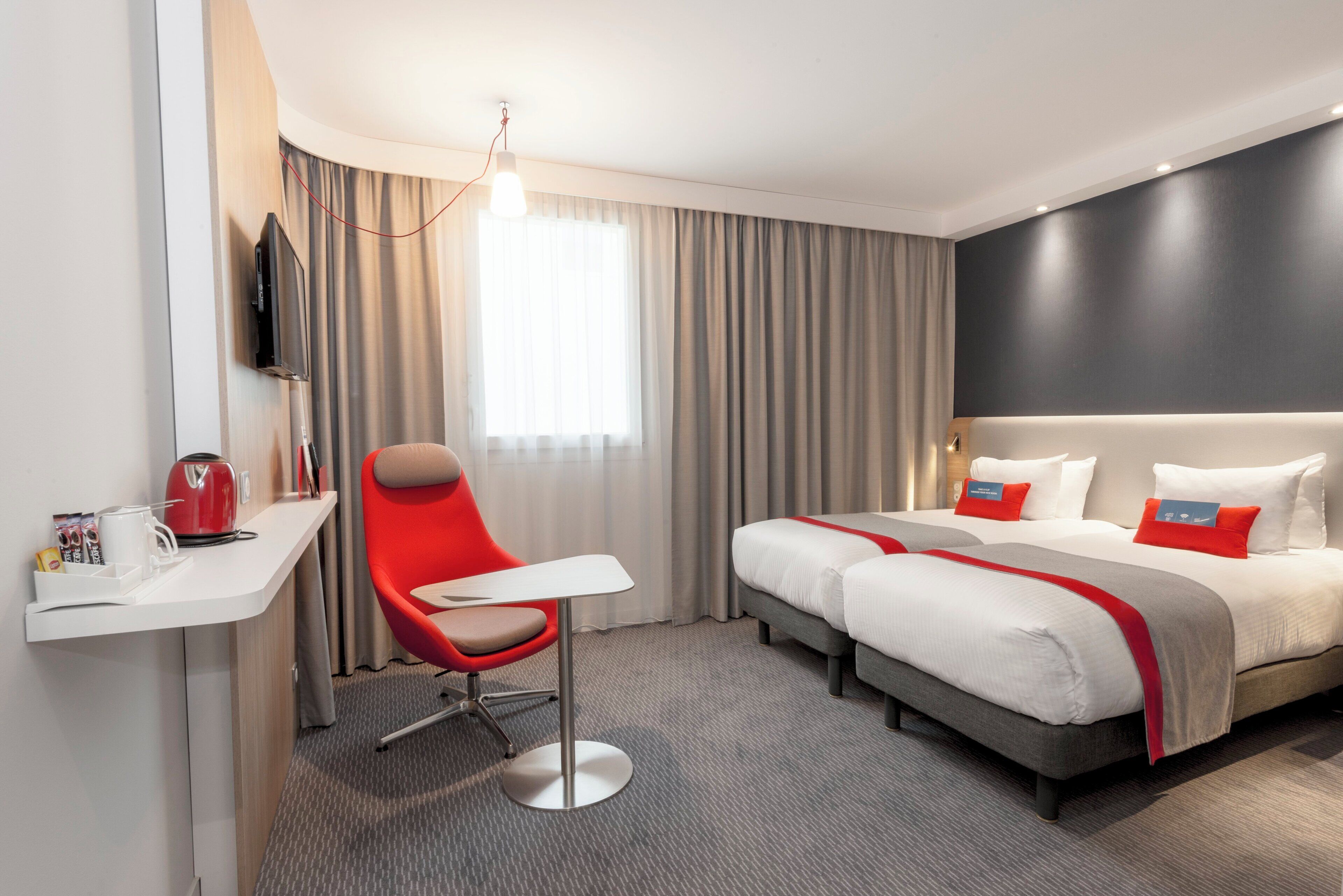 A hotel room with a bed, a desk, a chair, a TV, and a window with curtains.