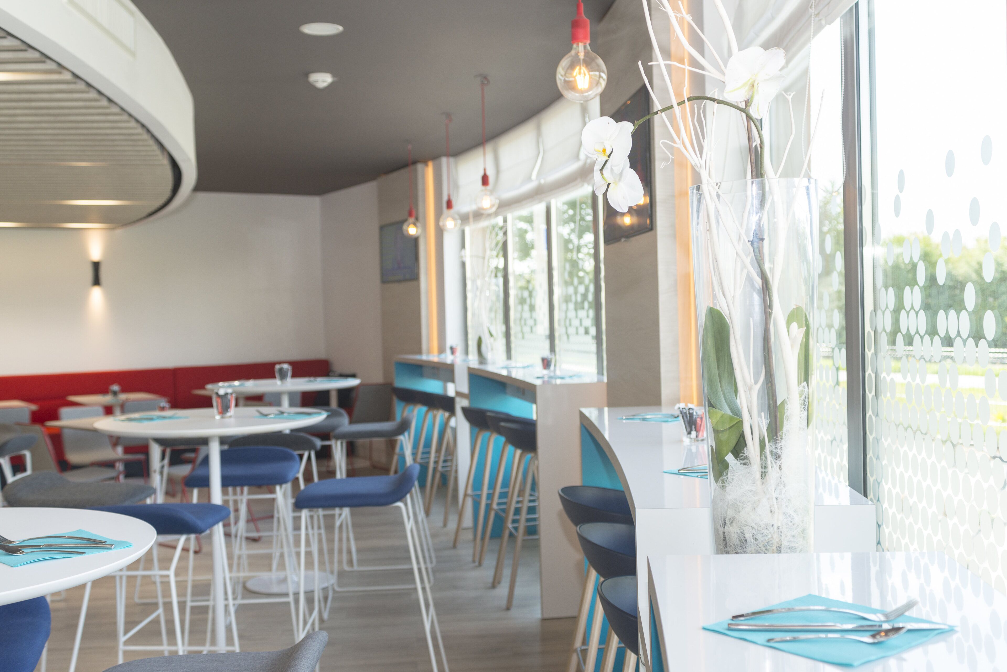 A modern restaurant interior with round tables, blue chairs, and a decorative plant arrangement.